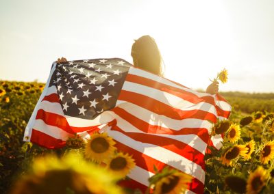 Beautiful,Girl,With,The,American,Flag,In,A,Sunflower,Field.