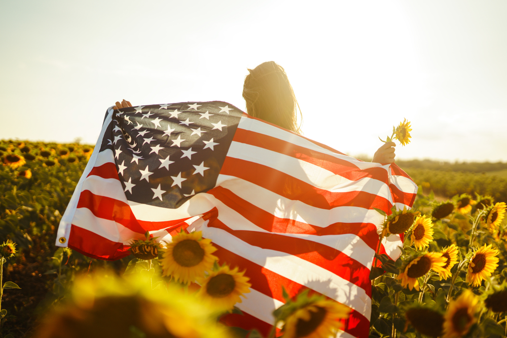 Beautiful,Girl,With,The,American,Flag,In,A,Sunflower,Field.