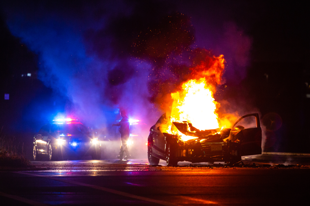 Car,On,Fire,At,Night,With,Police,Lights,In,Background