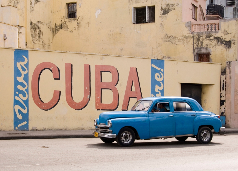 A,Vintage,1950’s,American,Car,Passing,A,’viva,Cuba’,Sign