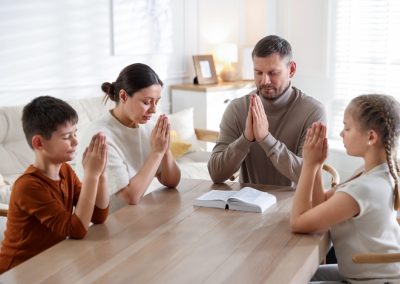 Family,With,Bible,Praying,At,Table,Indoors
