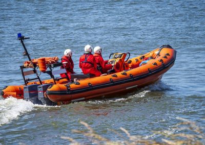 Three,Adults,Driving,An,Orange,Rescue,Boat,Through,The,Water,
