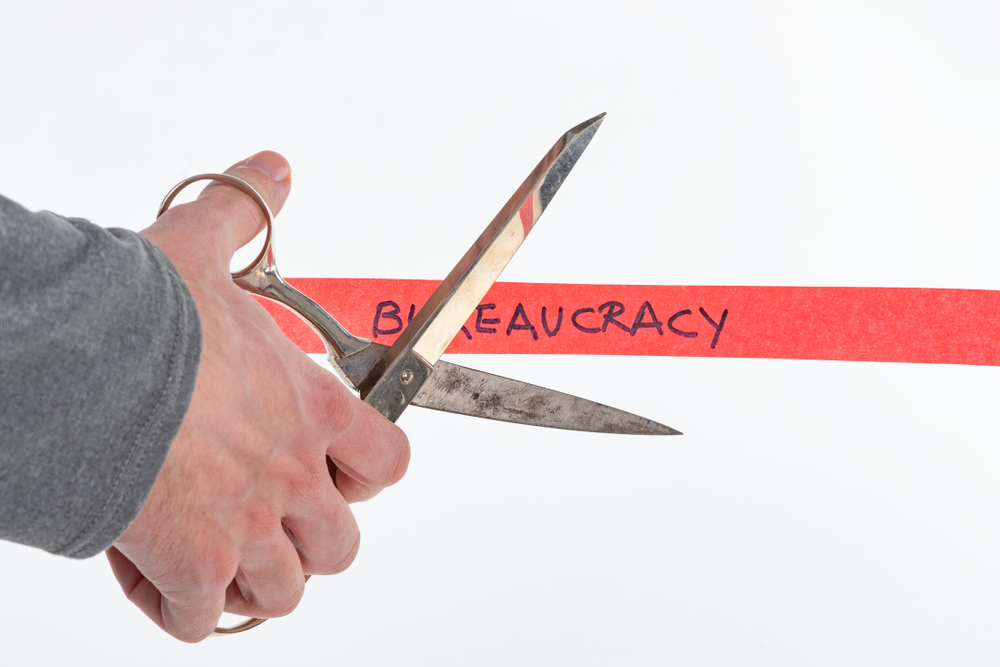 Male,Hand,Cutting,Through,Bureaucracy,Red,Tape,With,Scissors,Isolated